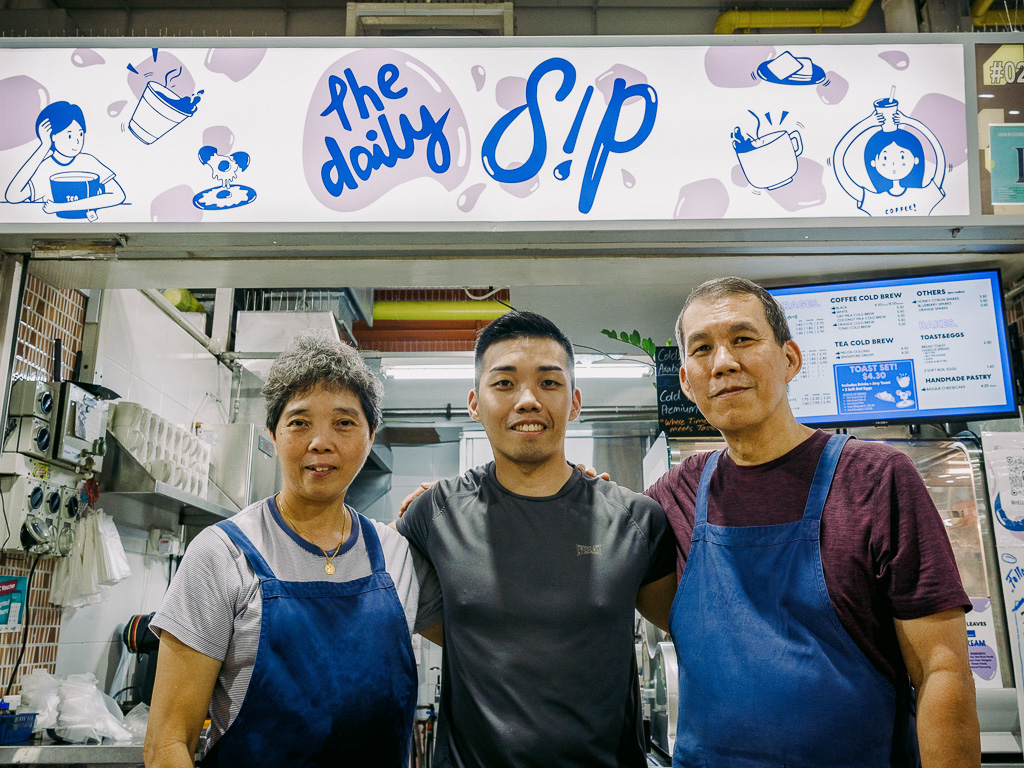 The Daily Sip’s stallfront with its logo and custom illustrations, with the Wong duo, and mum Mrs Wong (left). Photo: Ravin Thiruchelvam/HungryGoWhere the daily sip